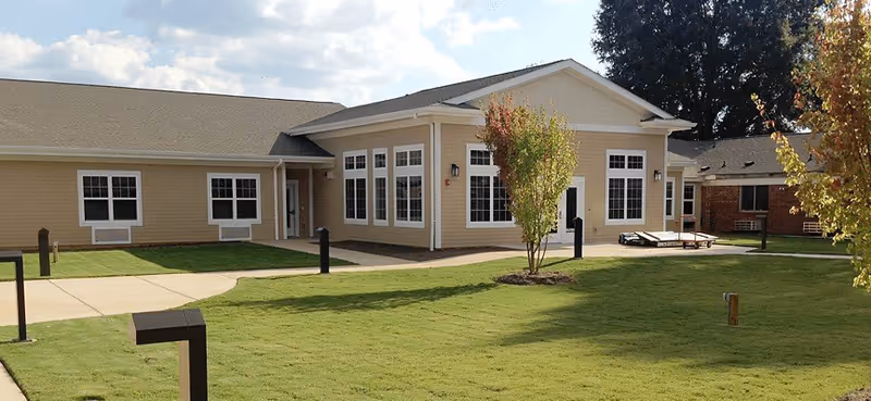 Exterior view of a single-story senior living facility with large windows and a green lawn.