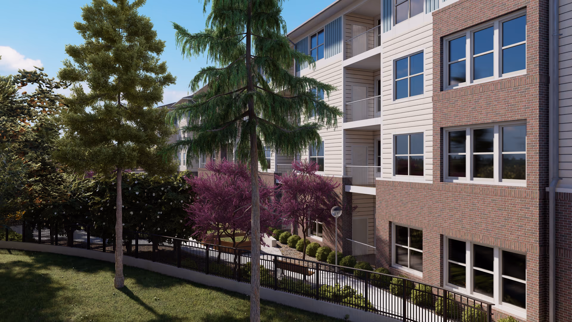 Exterior view of a multi-story senior living facility building with brick and siding facade, surrounded by trees and landscaping including green grass, purple flowering trees, and a black metal fence.