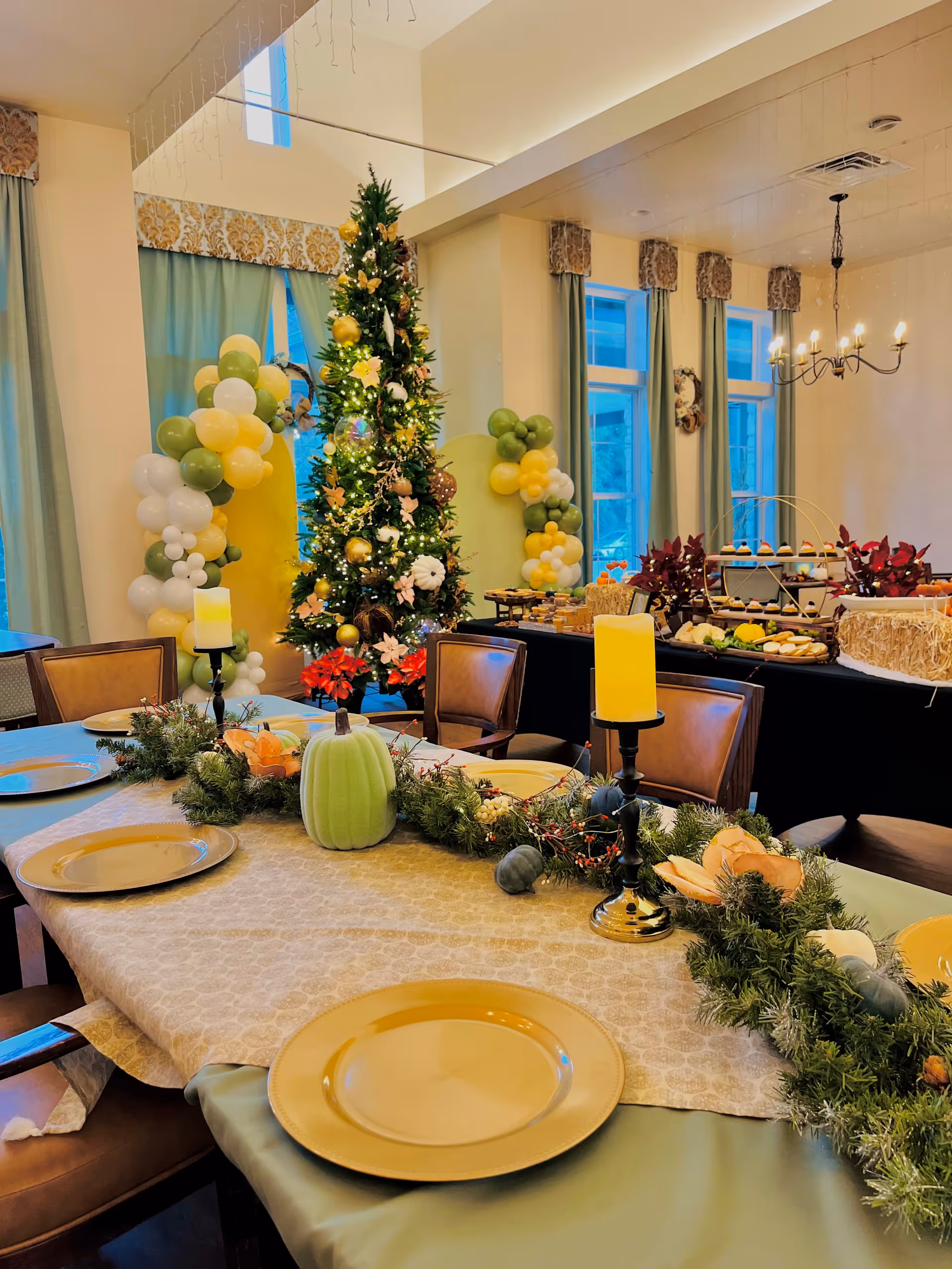 Festively decorated dining room with a Christmas tree, balloon arch, buffet, and a table set with gold chargers and seasonal centerpieces.