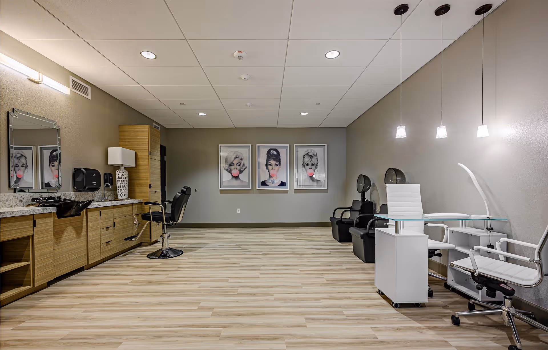 Spacious salon interior with styling chairs, manicure stations, wash sinks and three framed pop-art portraits on the back wall.
