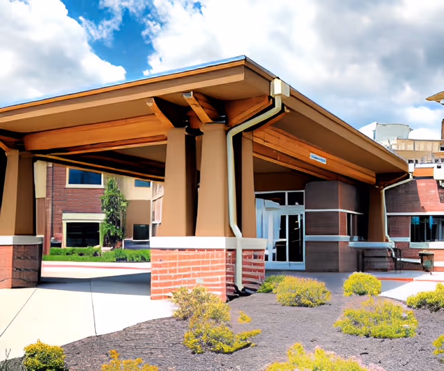 Covered entrance/porte-cochère of the Heritage Ridge building with brick columns, glass doors, and landscaped beds in front.