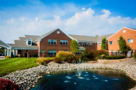 Brick senior living facility exterior with a pond, rocks, and manicured landscaping.