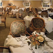 Formal dining room with round tables set with white tablecloths, floral centerpieces, and upholstered chairs.