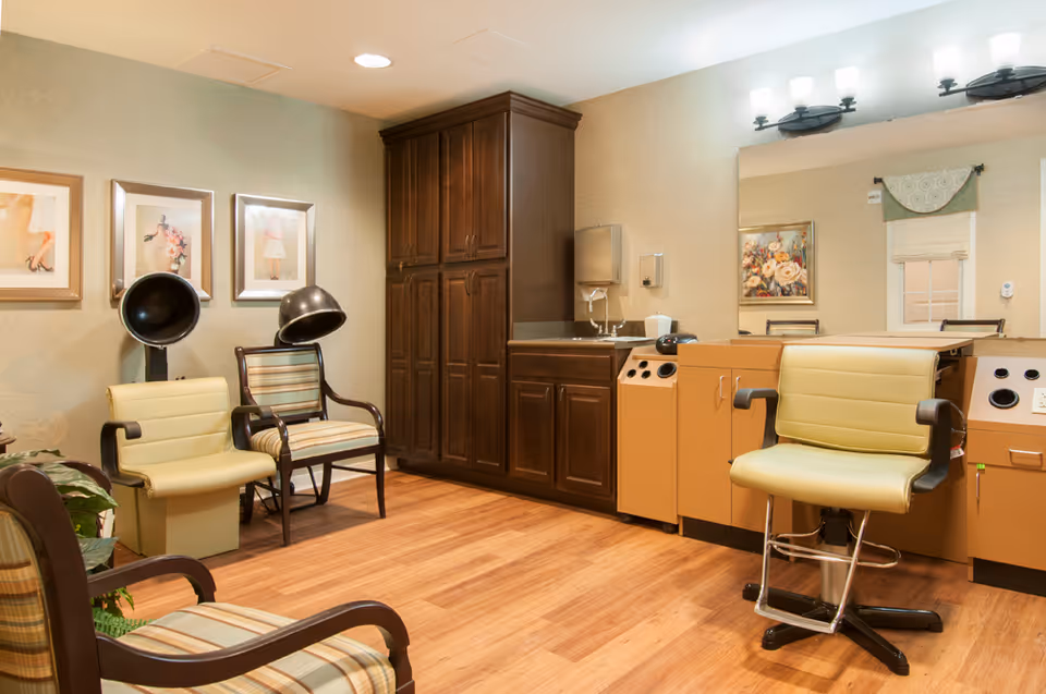 A well-lit salon-style room with styling chairs, hooded hair dryers, wooden cabinetry and a large mirror.