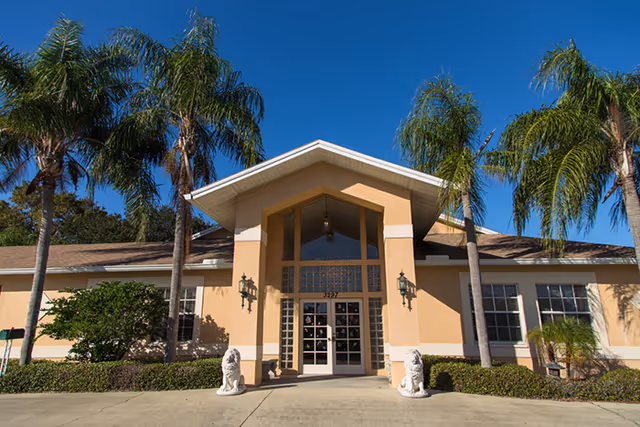 Exterior view of Evergreen Manor senior living facility entrance with palm trees and clear blue sky