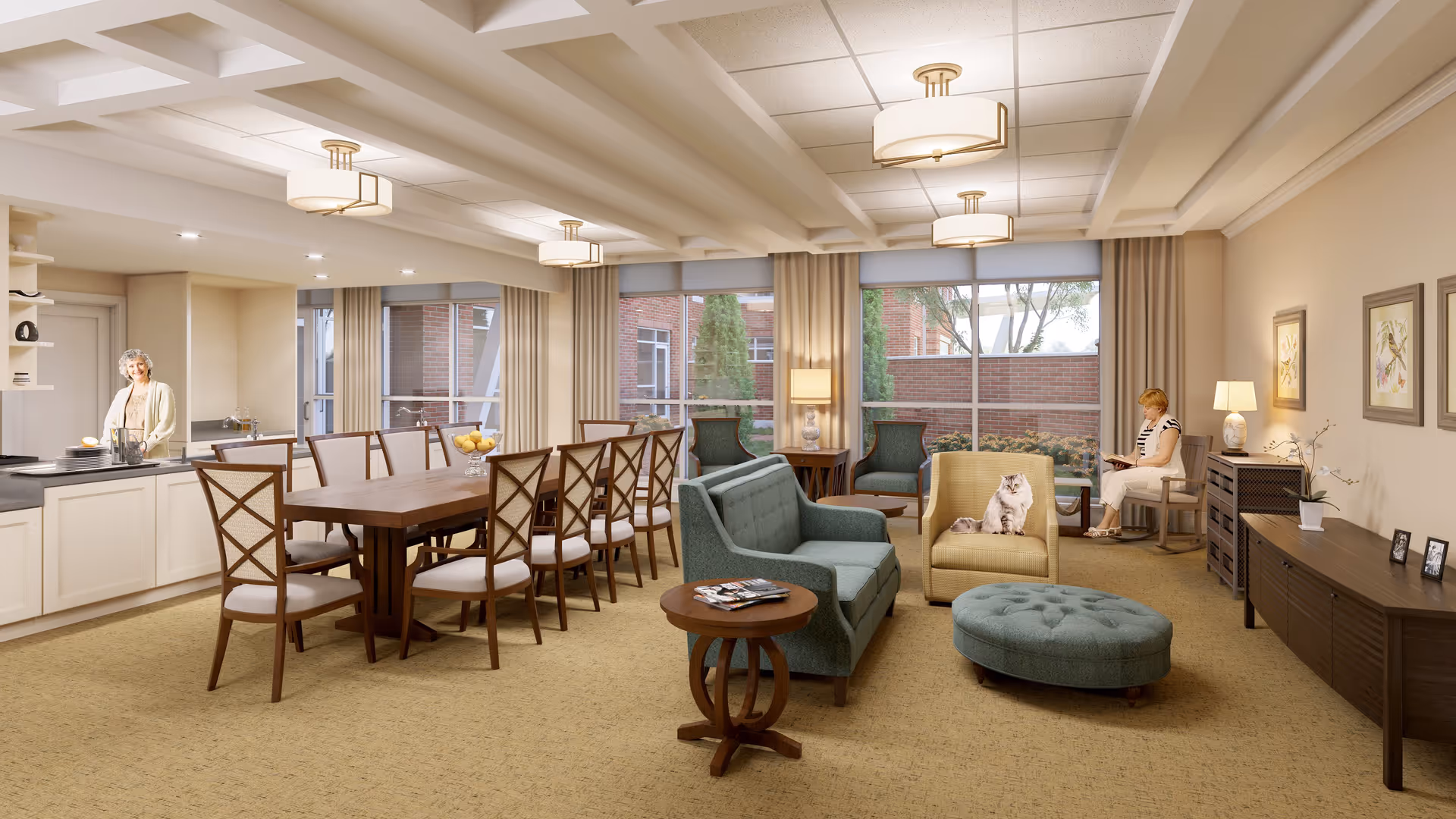 A spacious and well-lit assisted living common area featuring a kitchen with a woman standing near the counter, a long wooden dining table with chairs, and a cozy living room area with sofas, armchairs, an ottoman, and a cat sitting on one of the armchairs. A woman is seated in the corner reading a book. Large windows with beige curtains let in natural light and show a brick exterior with greenery outside.