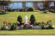 Front of a senior living facility with manicured lawn, flower beds, and a statue centerpiece.
