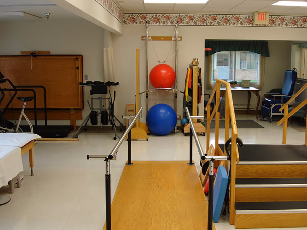 Physical therapy room with parallel bars, exercise balls, stairs, and various rehabilitation equipment.