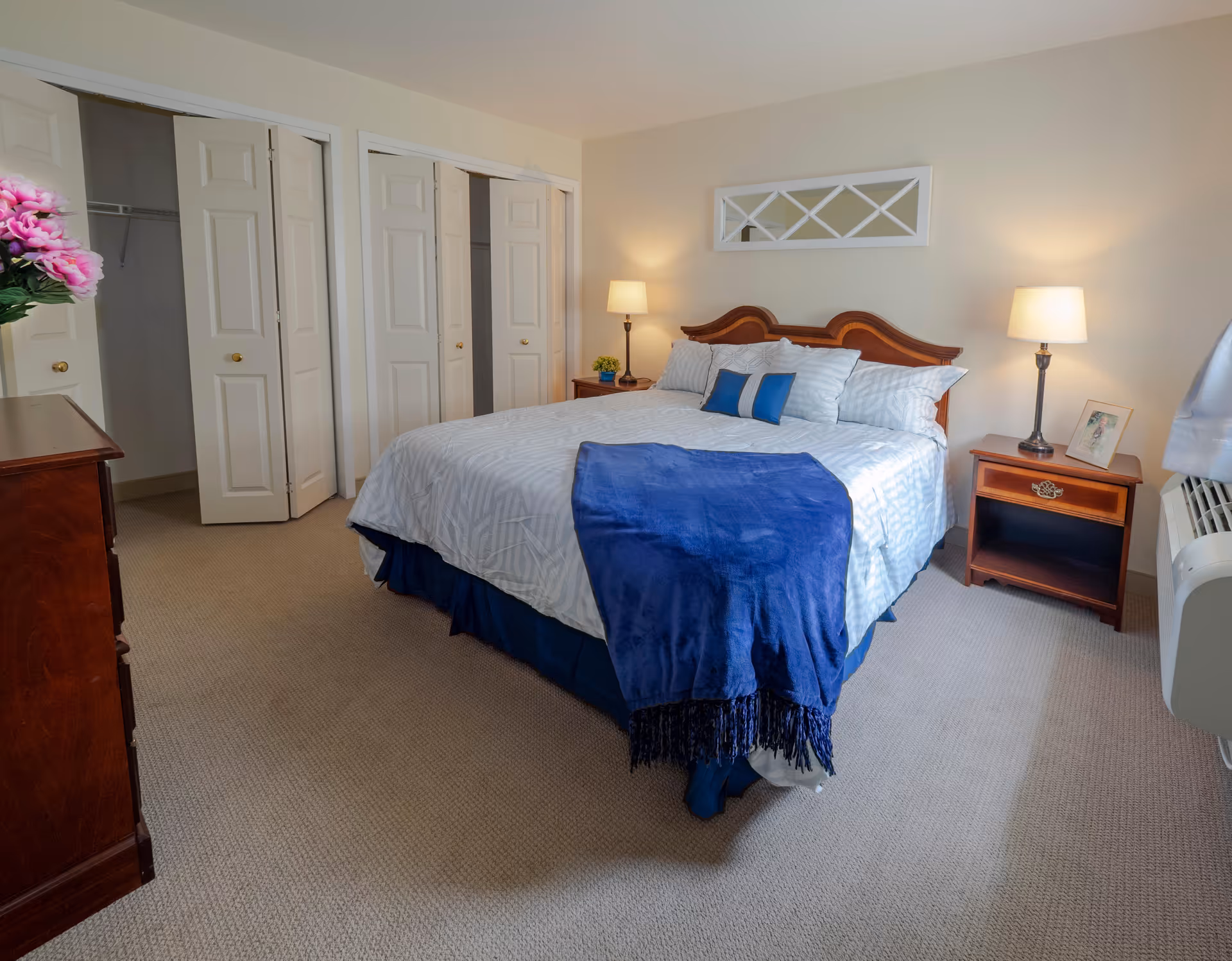 A neatly made bedroom with a double bed topped with blue accents, two bedside tables with lamps, and bi-fold closet doors.