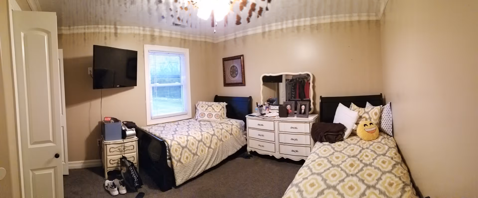 Shared bedroom with two twin beds, a dresser with mirror, a wall-mounted TV and a window.