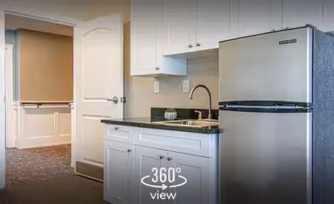 Compact kitchen area with white cabinets, stainless steel refrigerator, sink, and dark countertop.