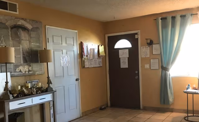 Interior entry area with a dark front door, adjacent white door, console table with lamps and decor, tiled floor and a window with teal curtains.