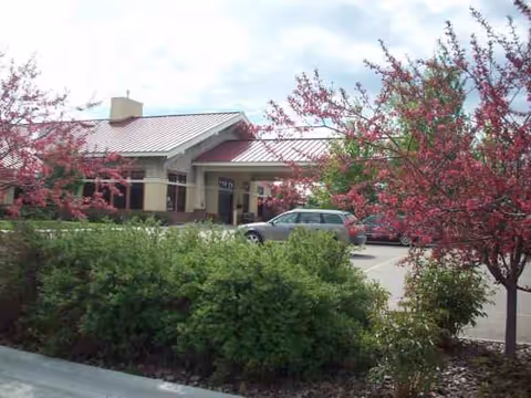 Exterior view of Ashton Living Center with pink blossoming trees and parked cars.