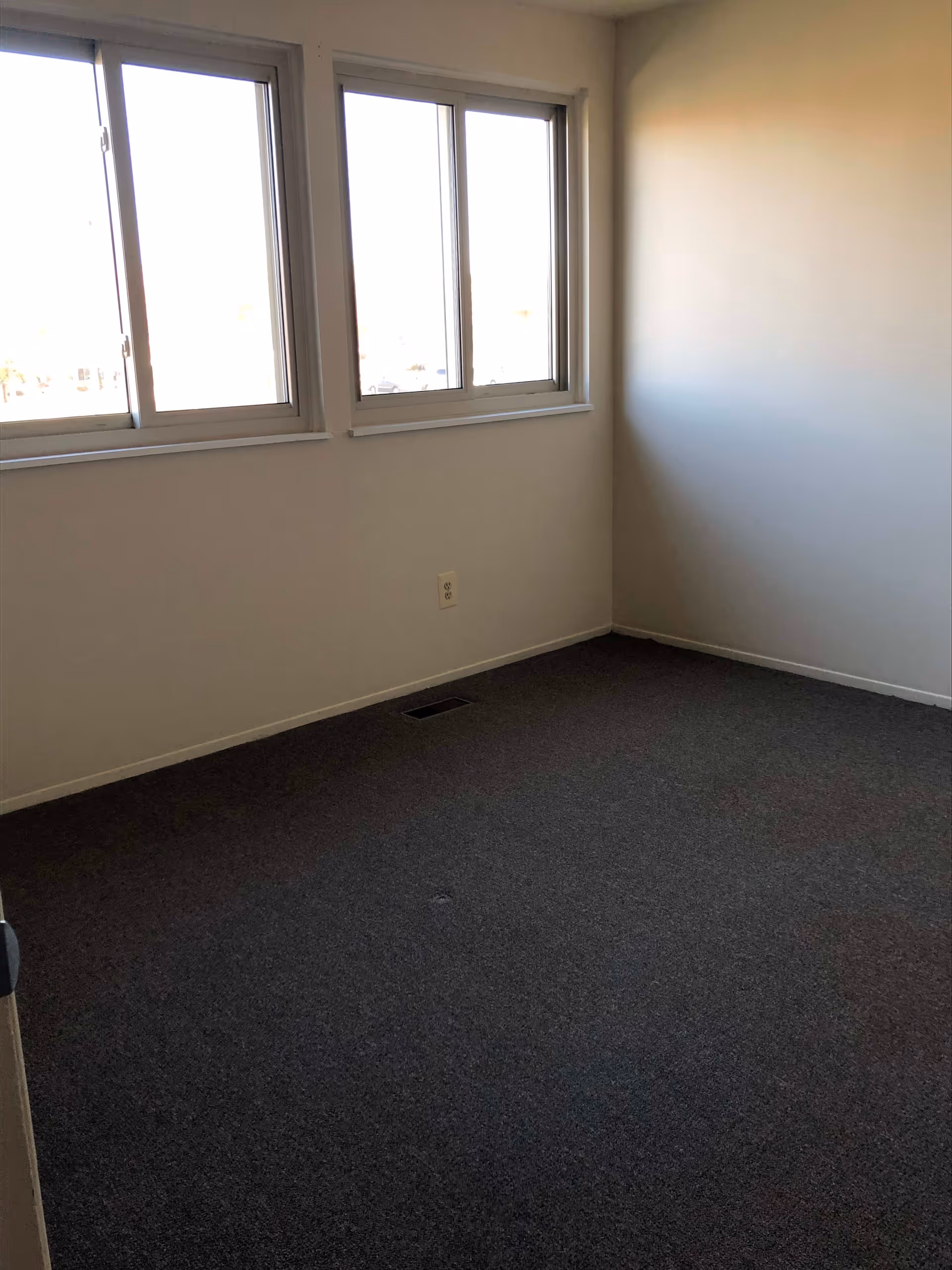 Small empty carpeted room with three windows on one wall and plain white walls.