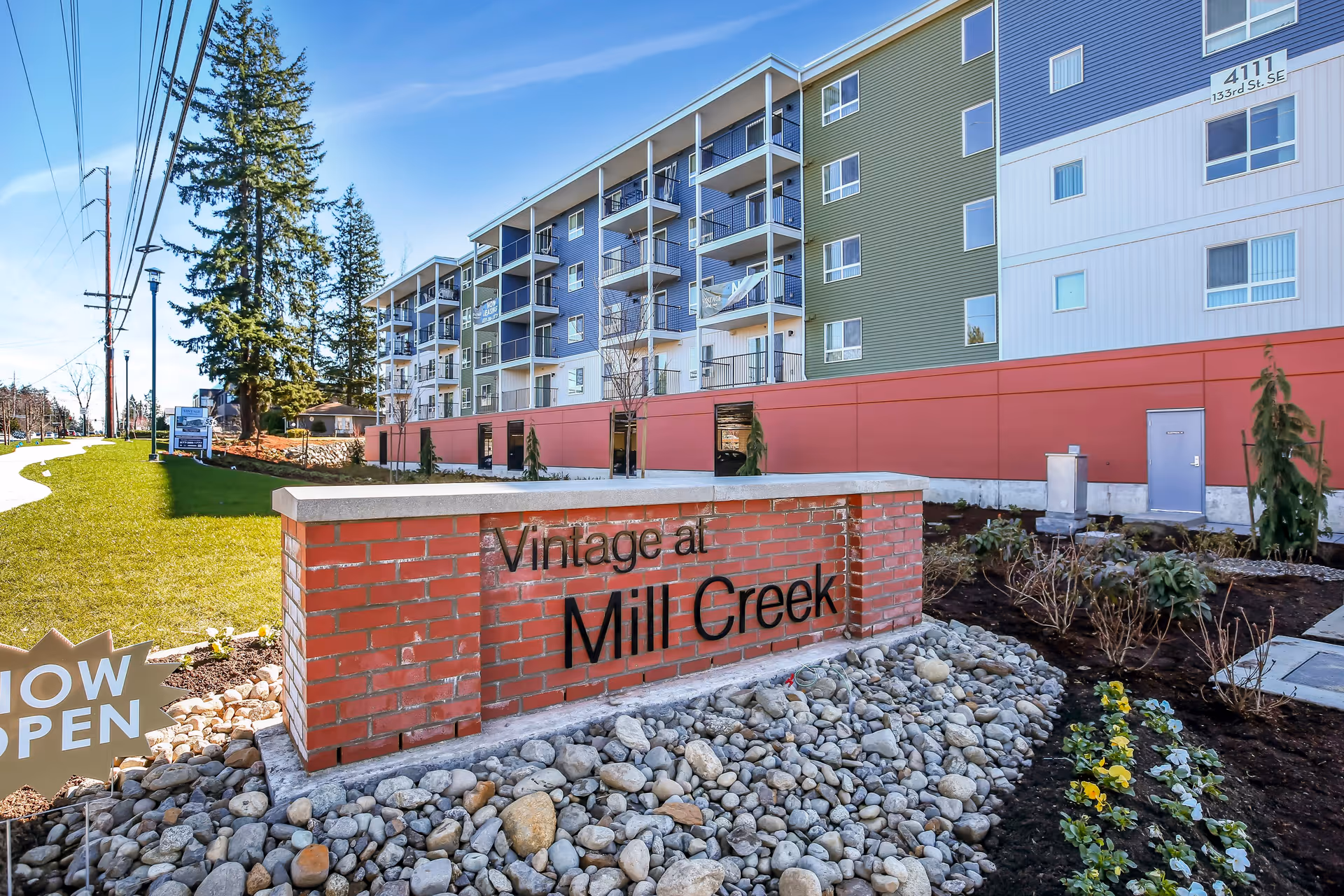 Exterior view of a multi-story residential building with balconies, a landscaped area with rocks and flowers, and a brick sign in the foreground that reads 'Vintage at Mill Creek'.