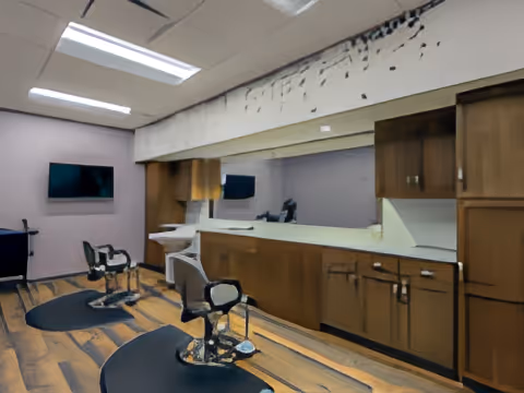 Interior salon area with two barber chairs, mirrors, a countertop and wooden cabinets.