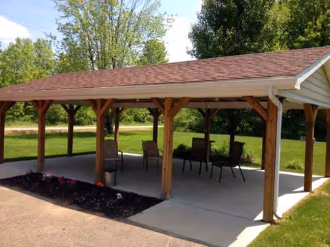 An outdoor covered seating pavilion with wooden posts and chairs.