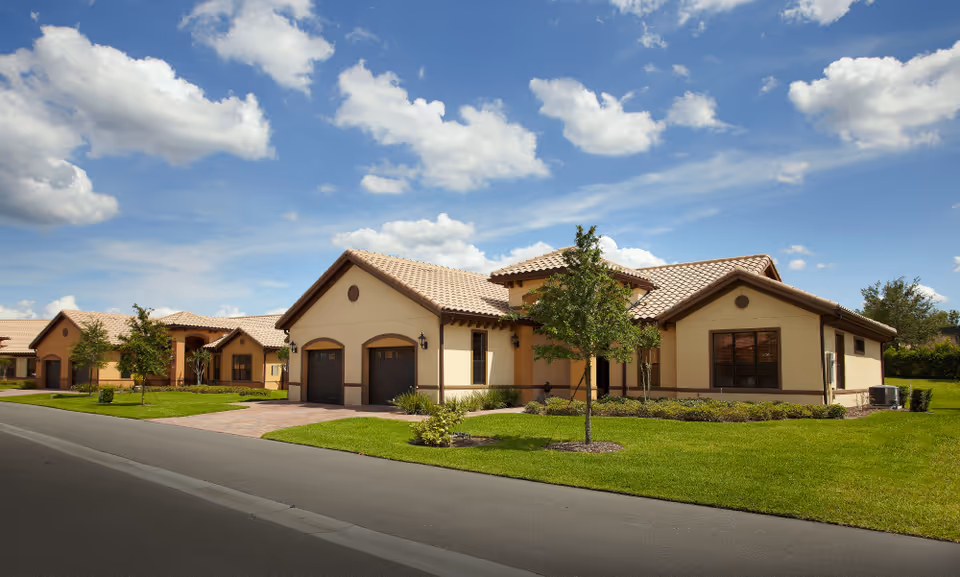 Sunlit front view of a tan, single-story senior living campus with green lawns.