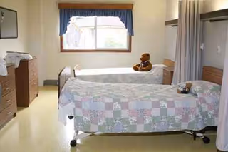 Two hospital beds with patchwork quilts occupy a bright Cortland Acres Nursing Home bedroom.