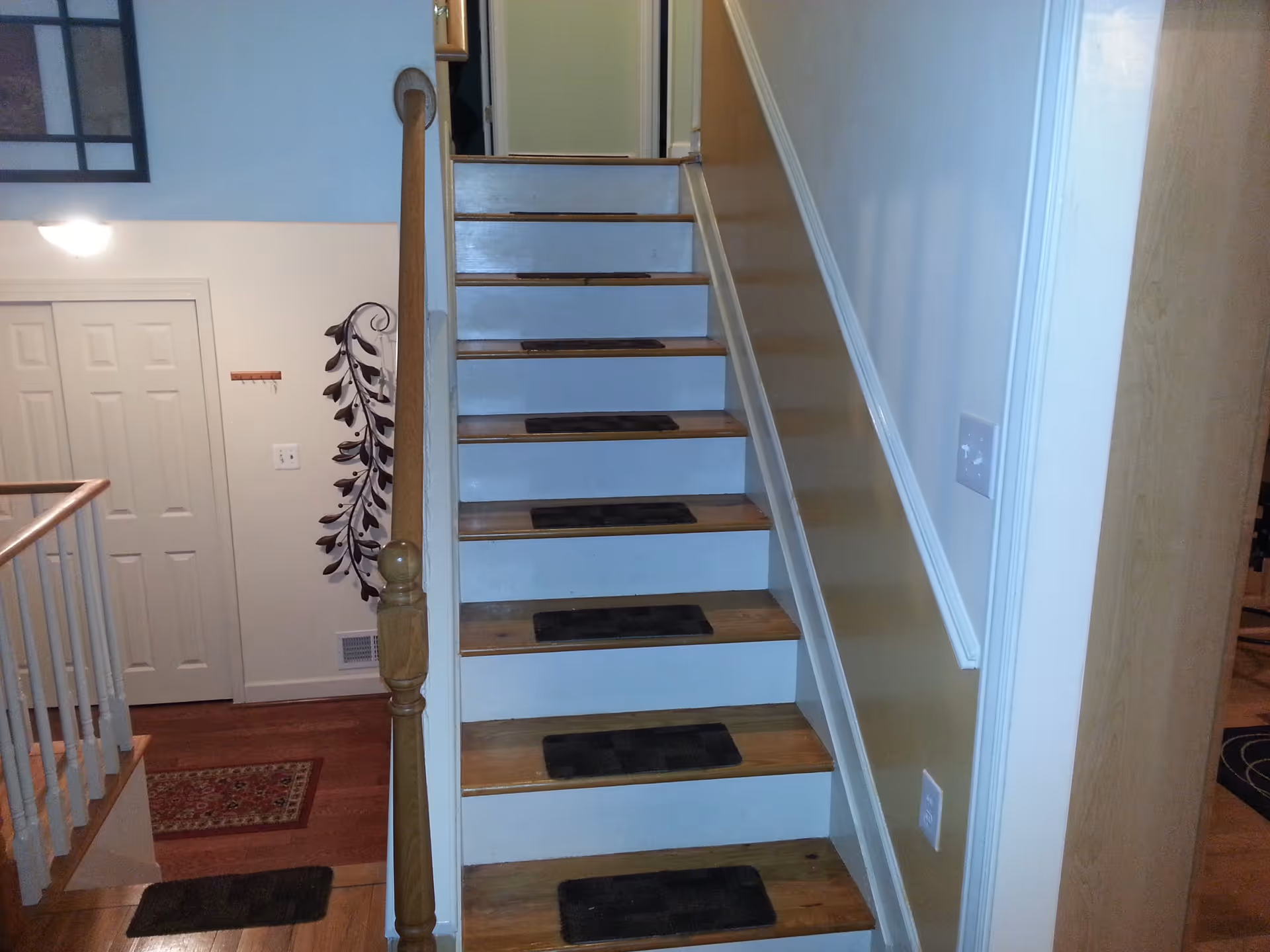 Interior view of a wooden staircase with non-slip treads, a handrail, and an adjacent hallway with closet doors and wall decor.