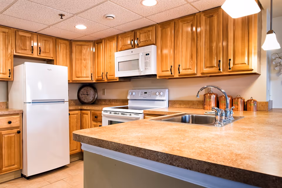 Bright wooden kitchen cabinets surround a white refrigerator, stove, microwave, and sink island.
