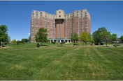Tall brick senior community building with a manicured green lawn and trees in front.