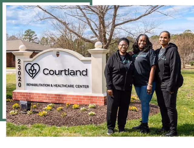 Three staff members stand outdoors beside the Courtland Rehabilitation and Healthcare Center sign.