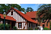 Exterior view of a building with Tudor-style architecture featuring white walls with dark wooden beams and a red tiled roof, surrounded by greenery and a streetlamp.