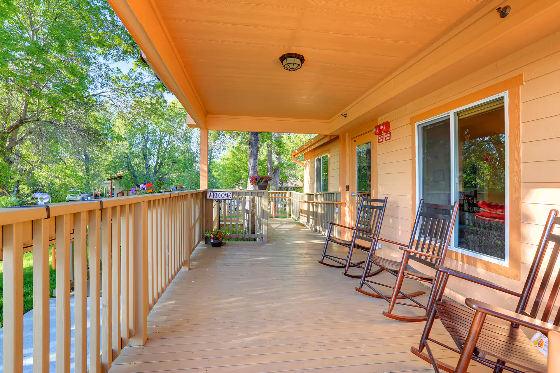 Covered wooden porch with several rocking chairs and a railing overlooking trees and a lawn.
