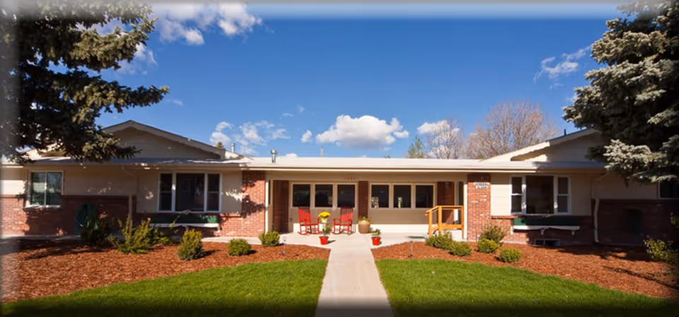 Front exterior of a single-story senior living facility with a central walkway and porch seating.