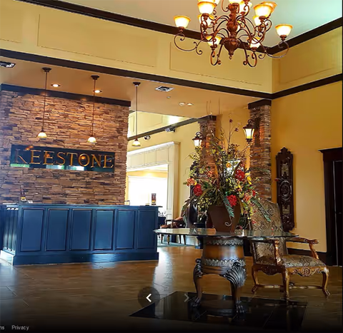 Keestone of Lawrenceburg lobby with blue reception desk, stone wall, chandelier, and floral arrangement.