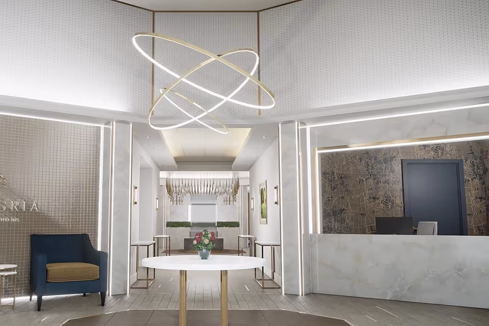 A modern and elegant reception area with a white marble front desk, a dark blue door behind the desk, a round white table with a flower vase in the center, a blue armchair with a brown cushion on the left, and contemporary lighting fixtures on the ceiling.