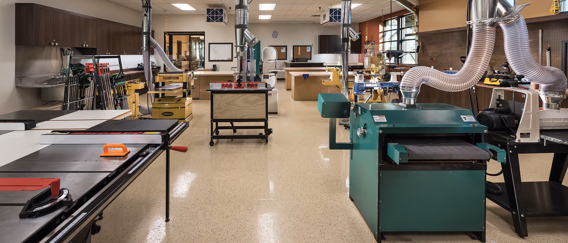 Well-equipped woodworking workshop with worktables, power tools, dust-collection ducts, and storage cabinets.