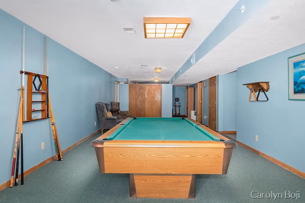 Basement game room with a pool table, cue rack, and seating against blue walls.