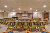 Small auditorium-style meeting room with rows of wooden chairs facing a podium and a projection screen at the front.