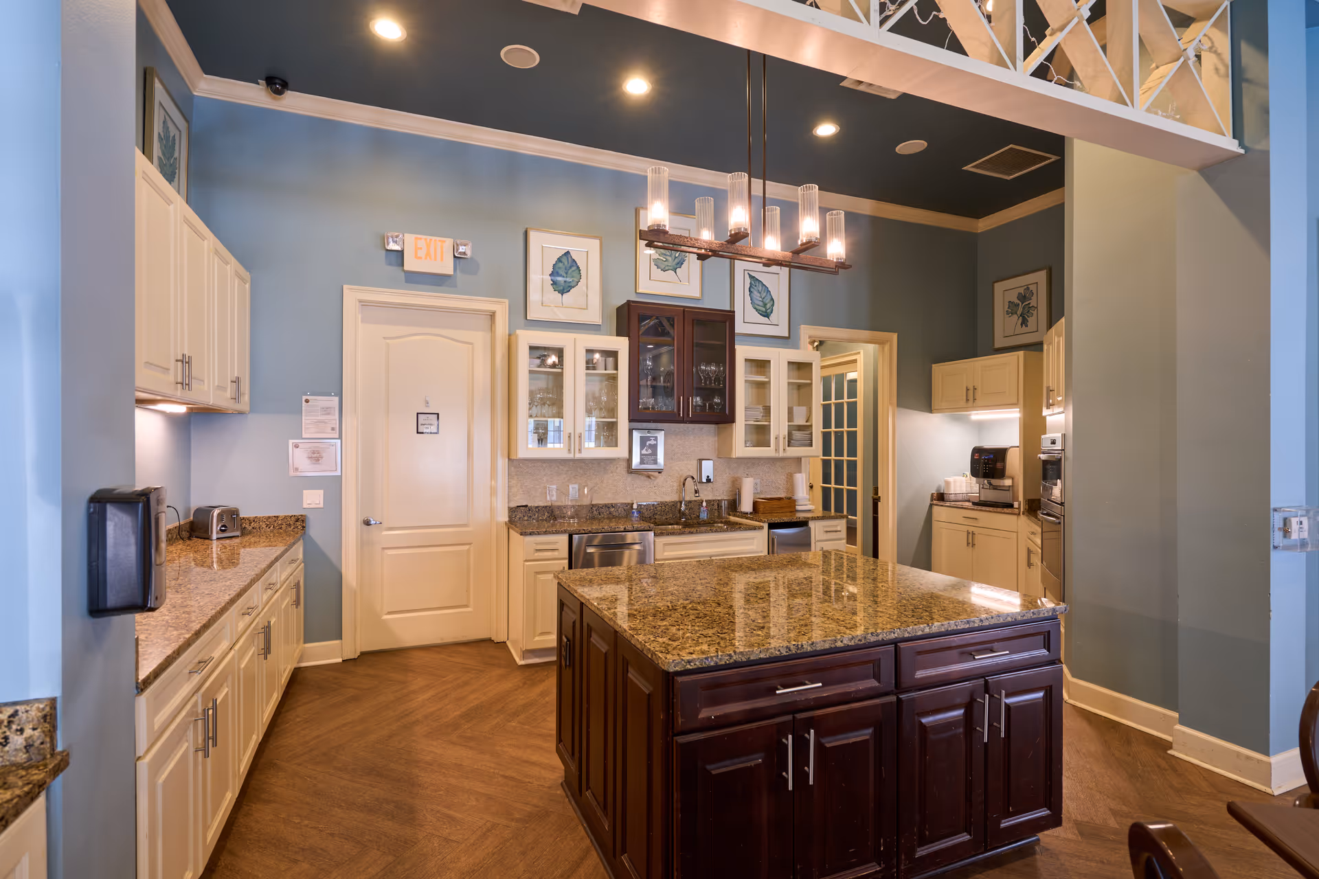 Communal kitchen featuring a large granite island, white cabinets, stainless appliances, and overhead chandelier lighting.