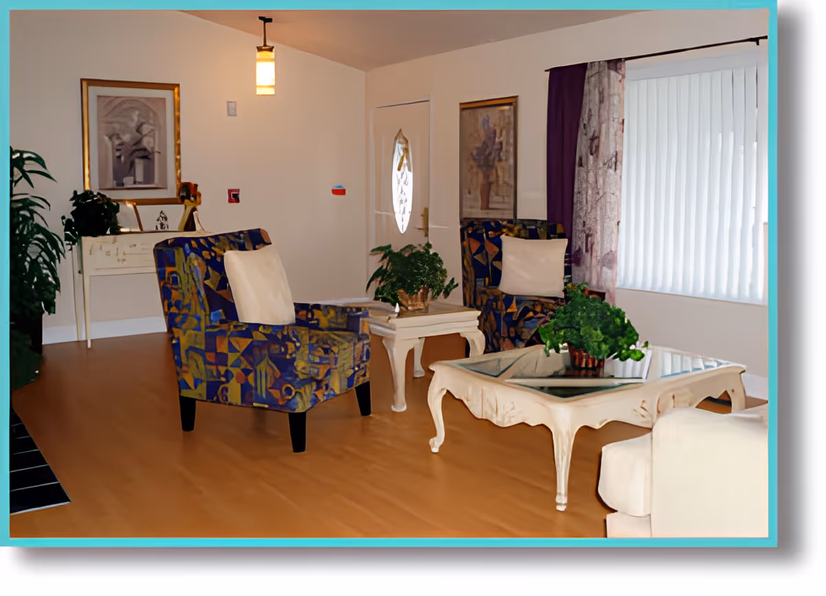 A cozy living room with two patterned armchairs with white cushions, a white coffee table with a glass top, a smaller side table with a plant, a white armchair, framed artwork on the walls, a hanging light fixture, and a window with vertical blinds and purple curtains.