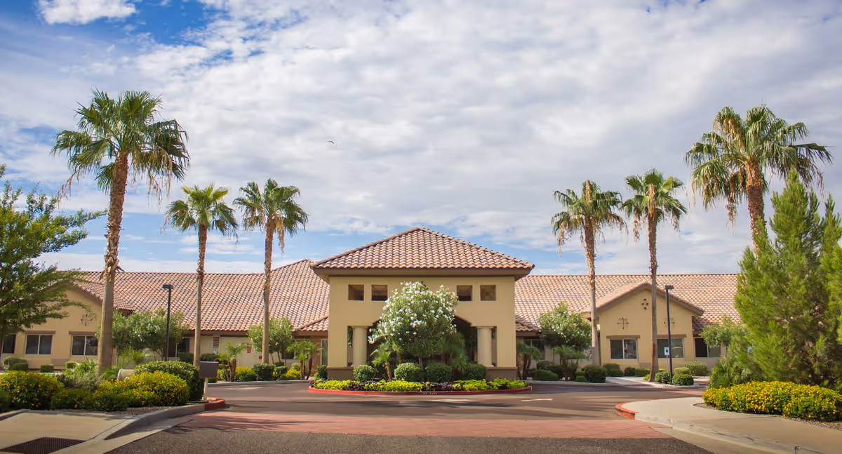 Sunny exterior of Silver Creek Inn senior living facility with palm trees and a circular driveway.