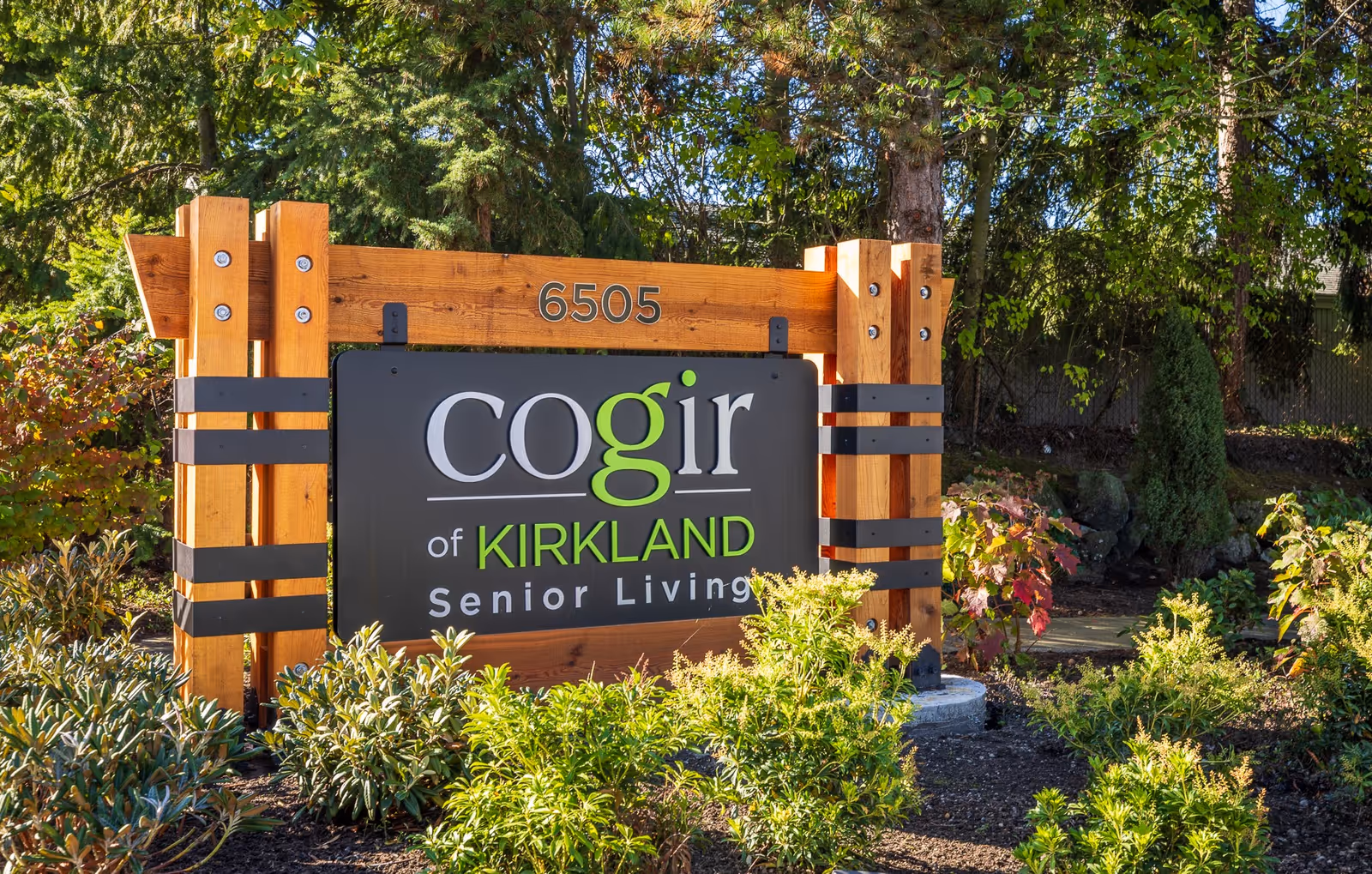 Outdoor wooden sign for Cogir of Kirkland Senior Living amid landscaping.