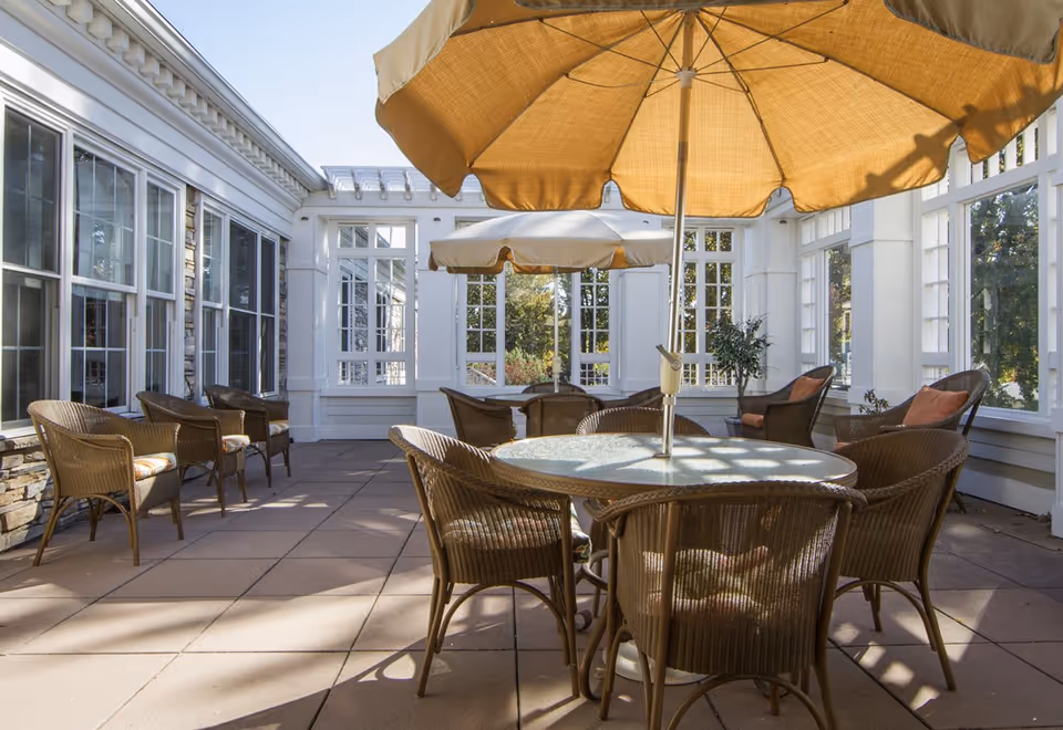 Sunlit enclosed patio with round tables, wicker chairs and large yellow umbrellas.