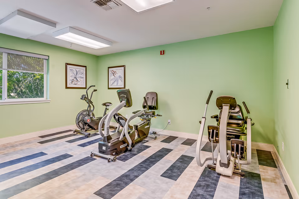 Small fitness room with several stationary and recumbent exercise bikes against green walls and a patterned floor.
