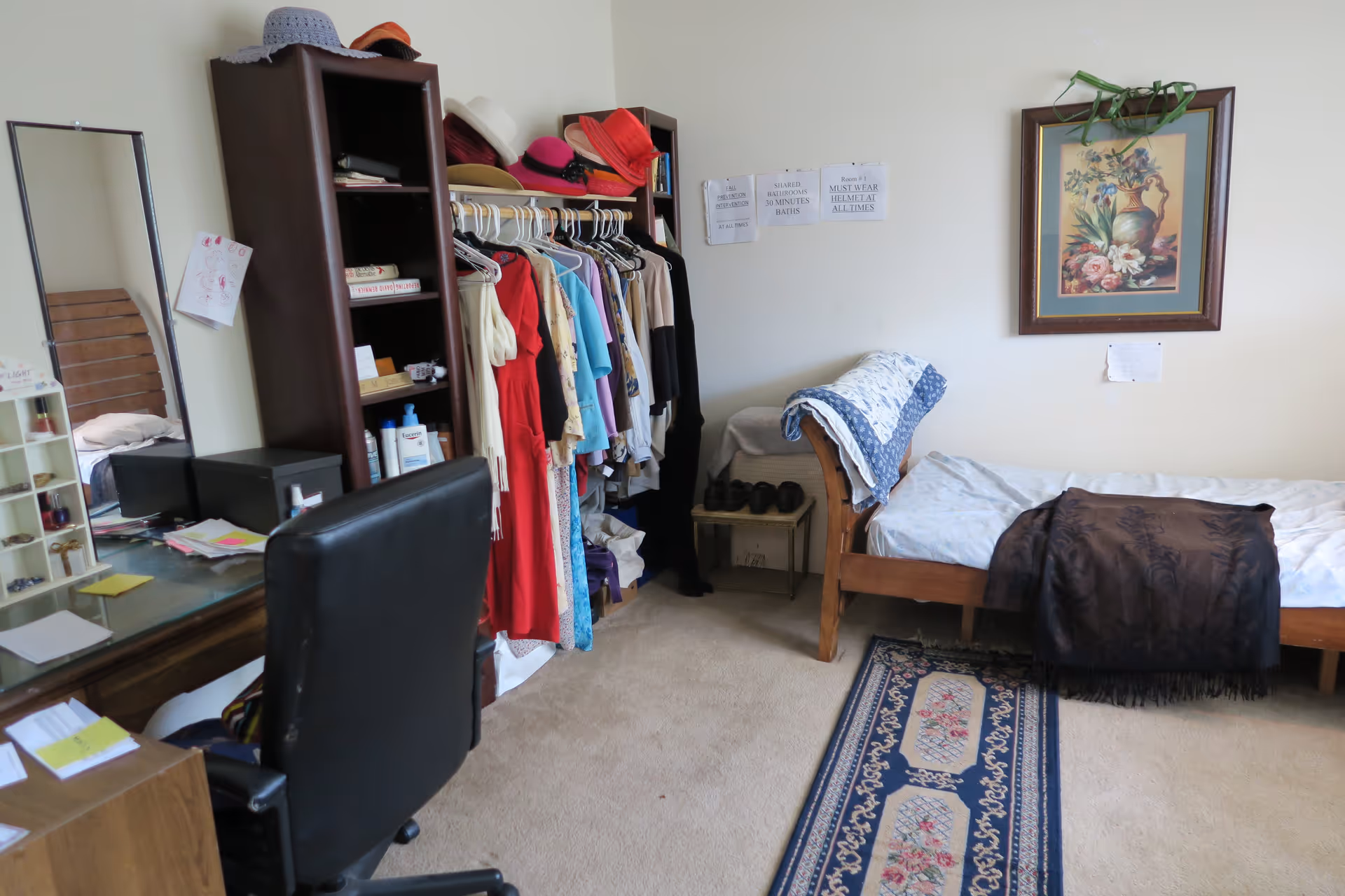 A tidy bedroom with a single bed, rug, clothing rack, shelving and a desk with a chair.