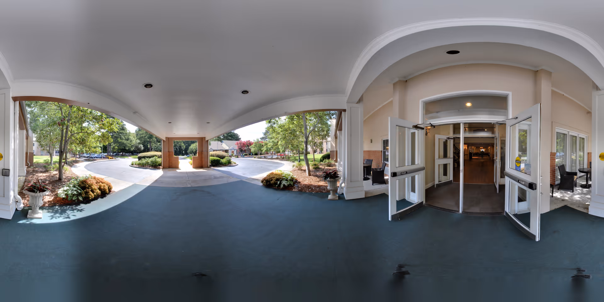 Covered front entrance/porte-cochère with open double doors leading into a senior living facility and a landscaped driveway.