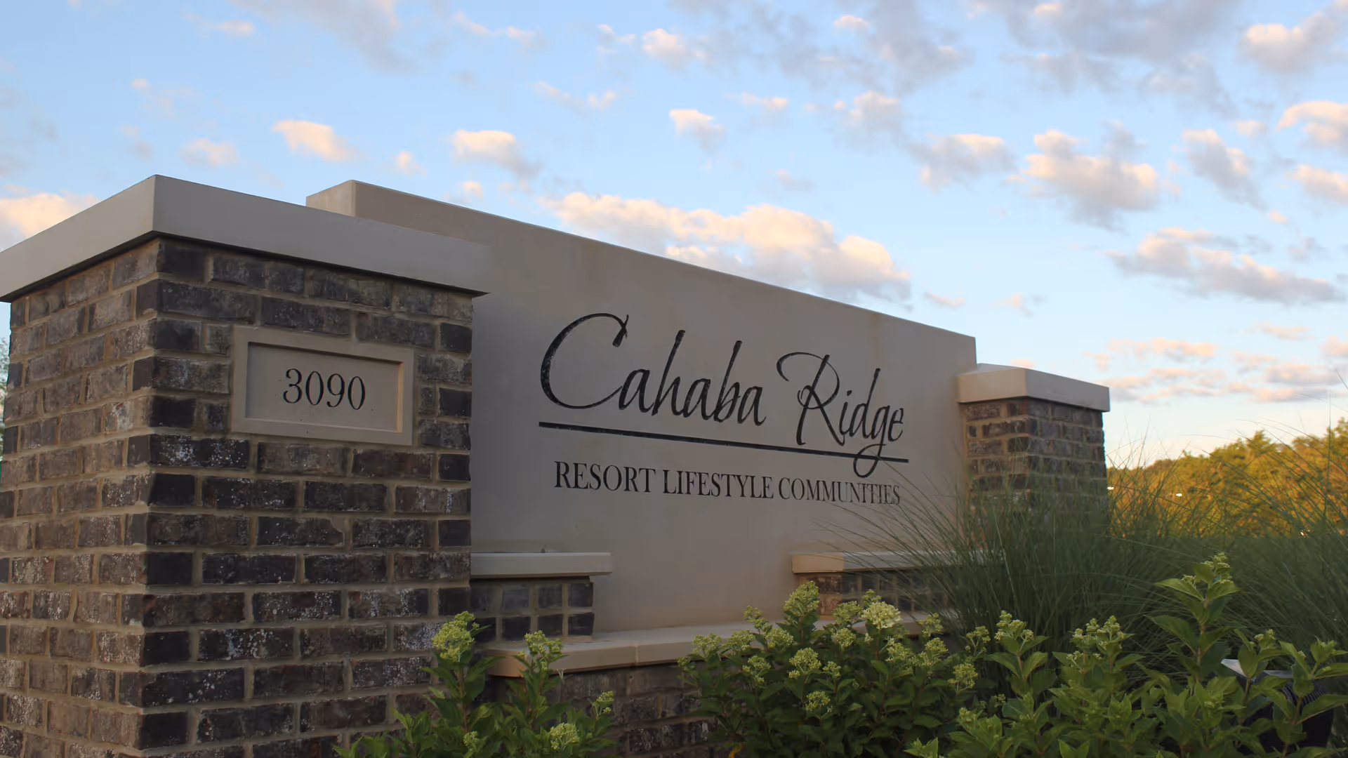 Outdoor stone and concrete sign for Cahaba Ridge Resort Lifestyle Communities with the address number 3090, surrounded by greenery and under a partly cloudy sky.