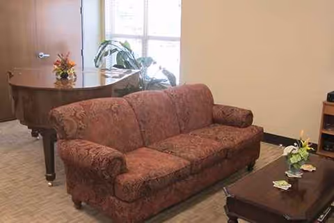 Red patterned sofa, coffee table, and piano in a cozy senior living lounge.