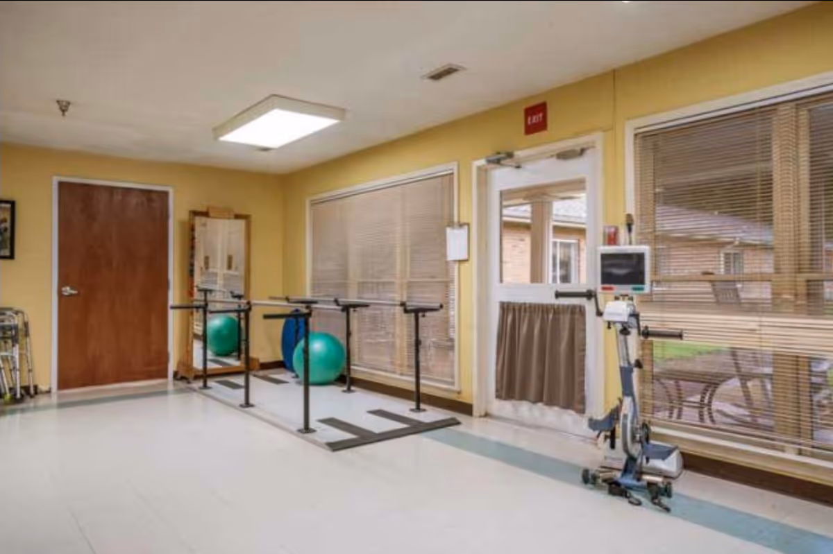 Indoor rehabilitation room with parallel bars, exercise balls, and a stationary bike.