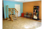 Small interior therapy room with a wooden practice staircase, chairs, and exercise equipment against blue and orange walls.