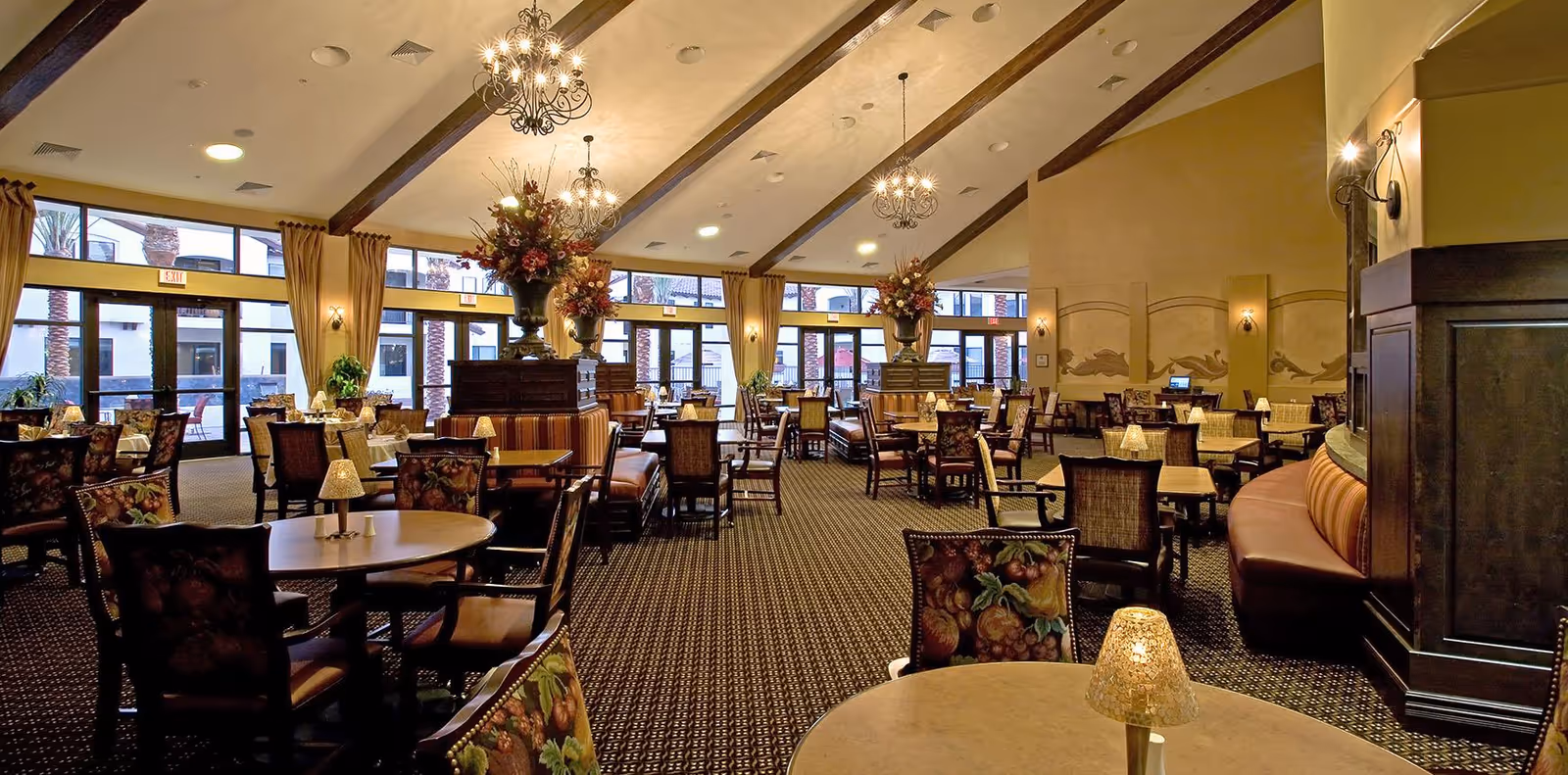 Spacious elegant dining room with multiple tables and upholstered chairs under chandeliers and large windows.