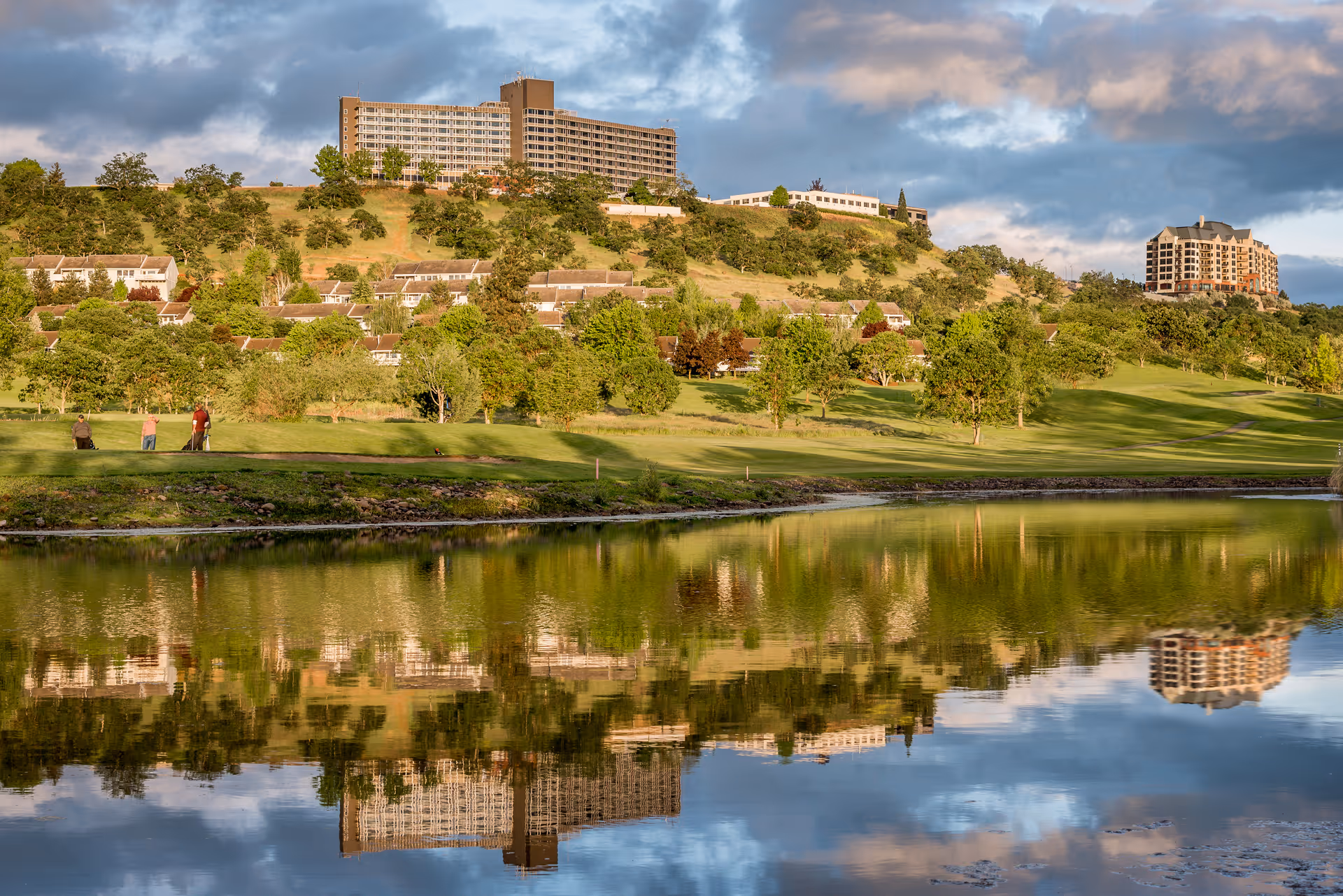 Rogue Valley Manor hillside campus with trees, lawns, and a lake reflection.