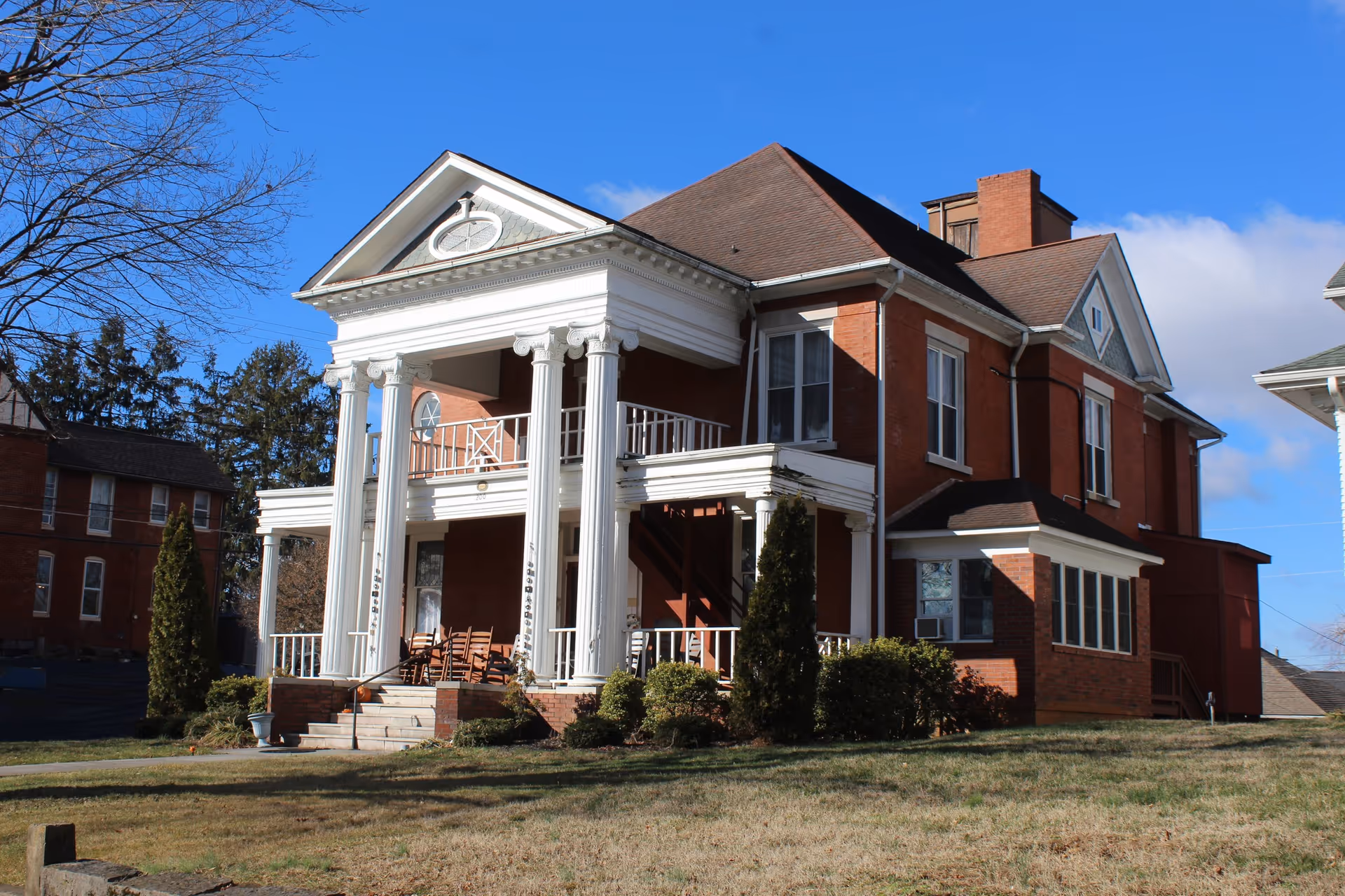 Brick two-story building with a grand white-columned front porch and manicured landscaping.